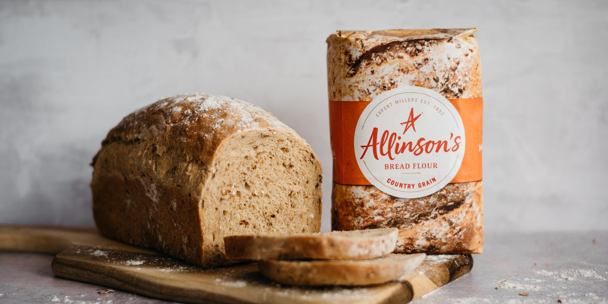 Farmhouse Country Grain Loaf sliced on a serving board, next to a bag of Allinson's Country Grain flour
