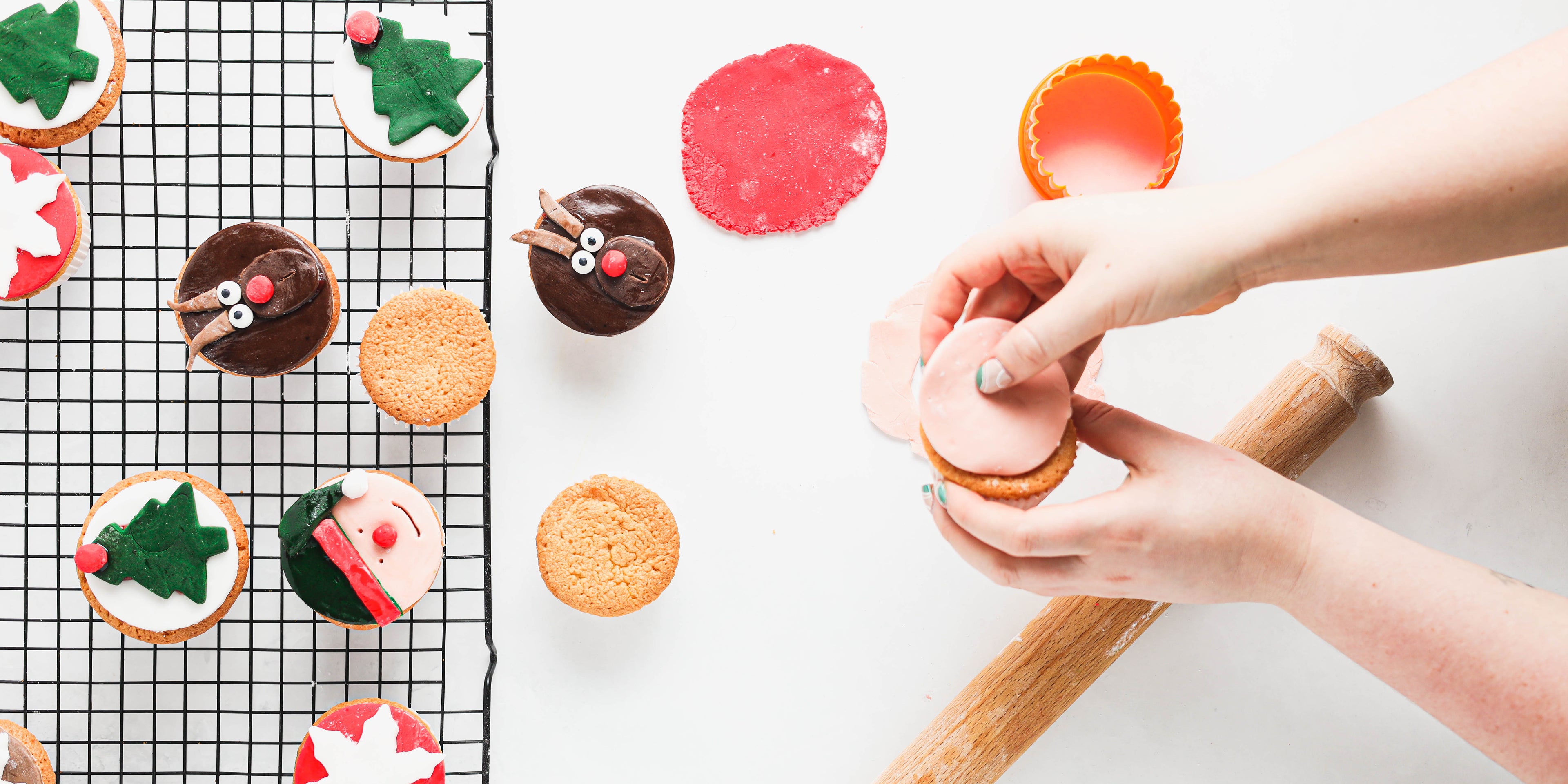 Christmas Cupcakes on a wire rack, next to hands making the fondant topping decoration