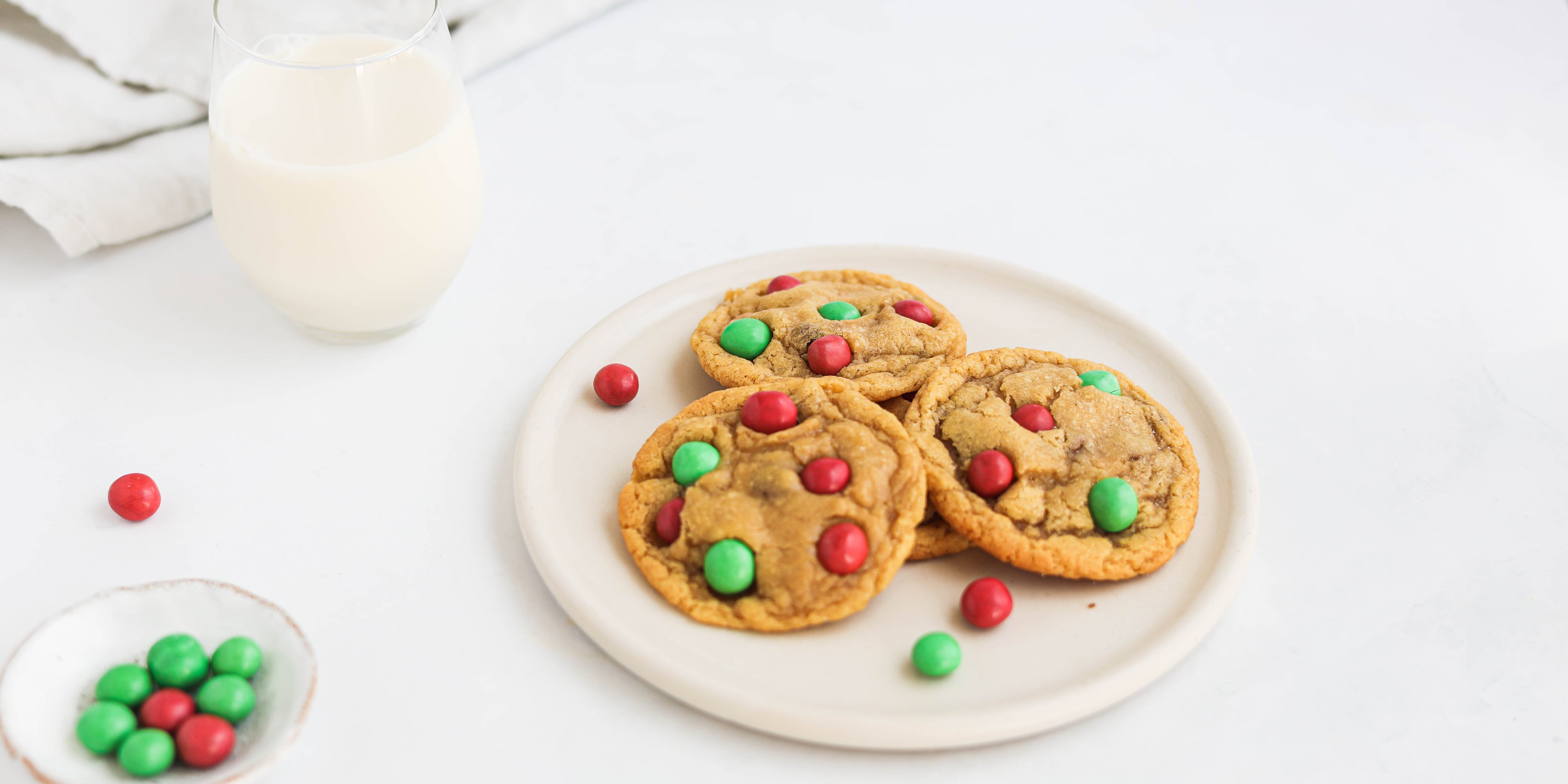 Copycat Millies Cookies Elf Style next to a glass of milk and dish of red and green m&ms