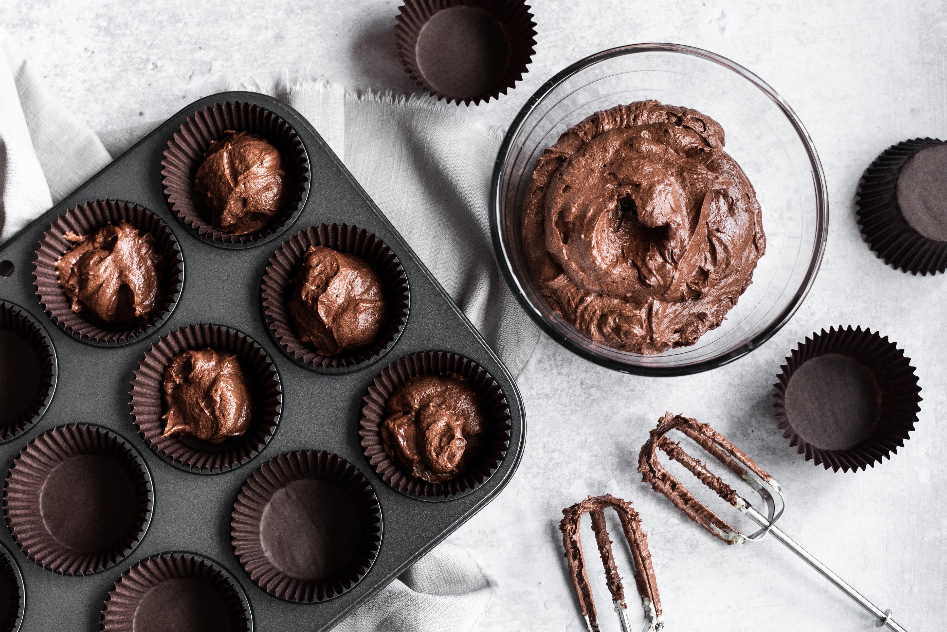 Flat lay of Mary Berry Cupcakes, with a bowl of chocolate cake batter mix, and whisks.