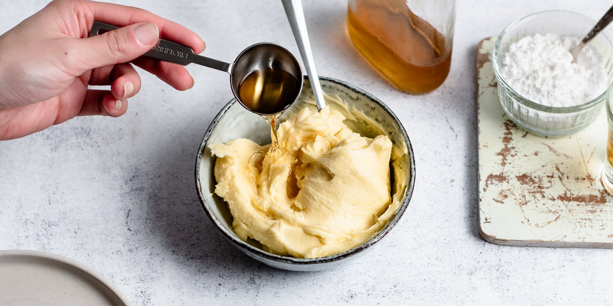 Top view of creamed butter in a bowl adding a measure of brandy with a hand holding the scoop