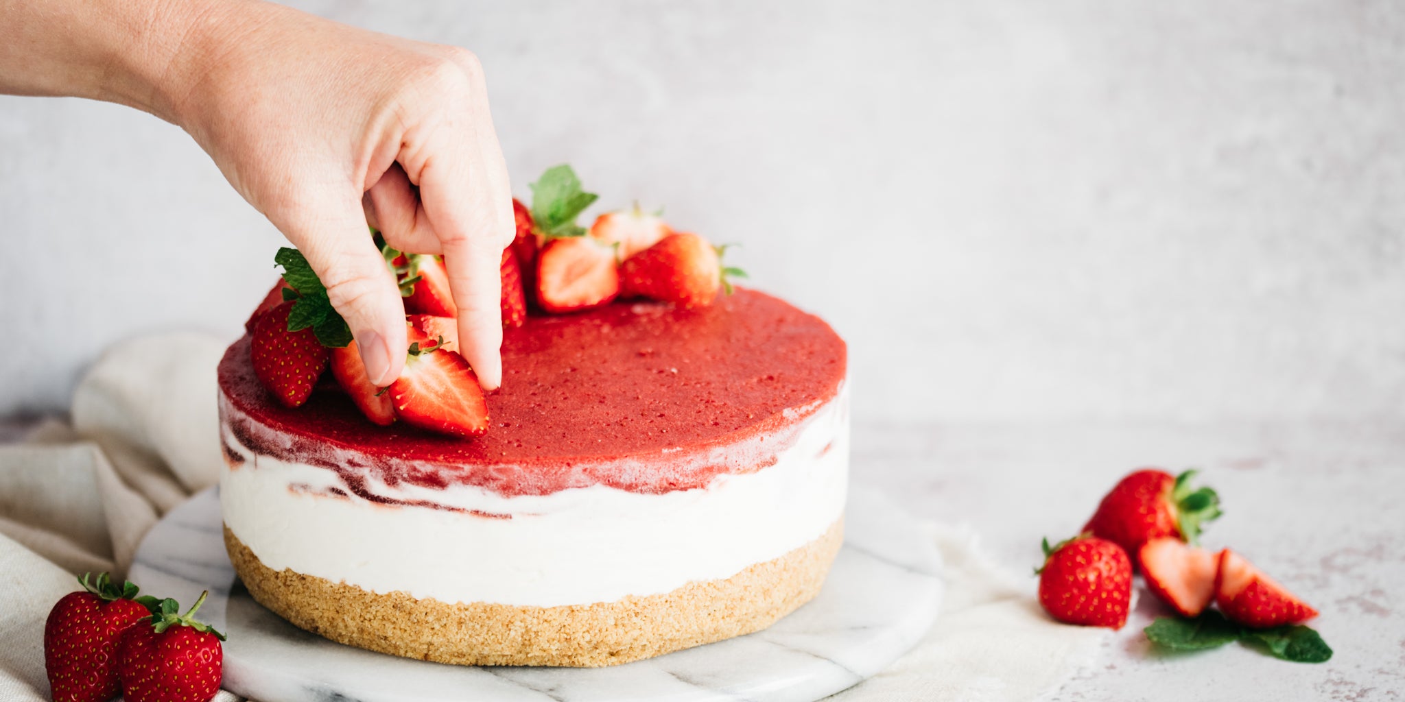 Hand placing strawberry on top of cheesecake
