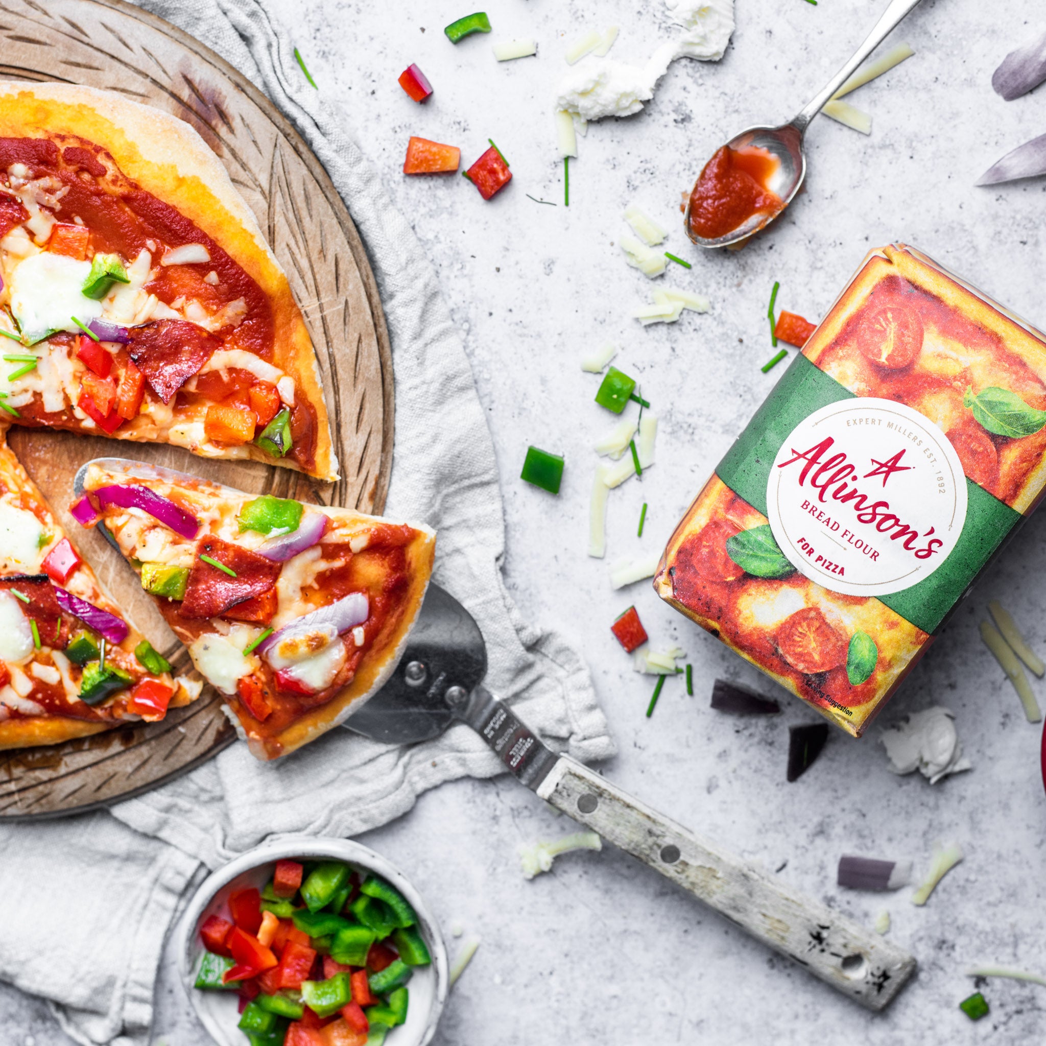 A top down view of a pizza slice taking a slice of allinsons pizza next to a pack of allinson's bread flour for pizza dough