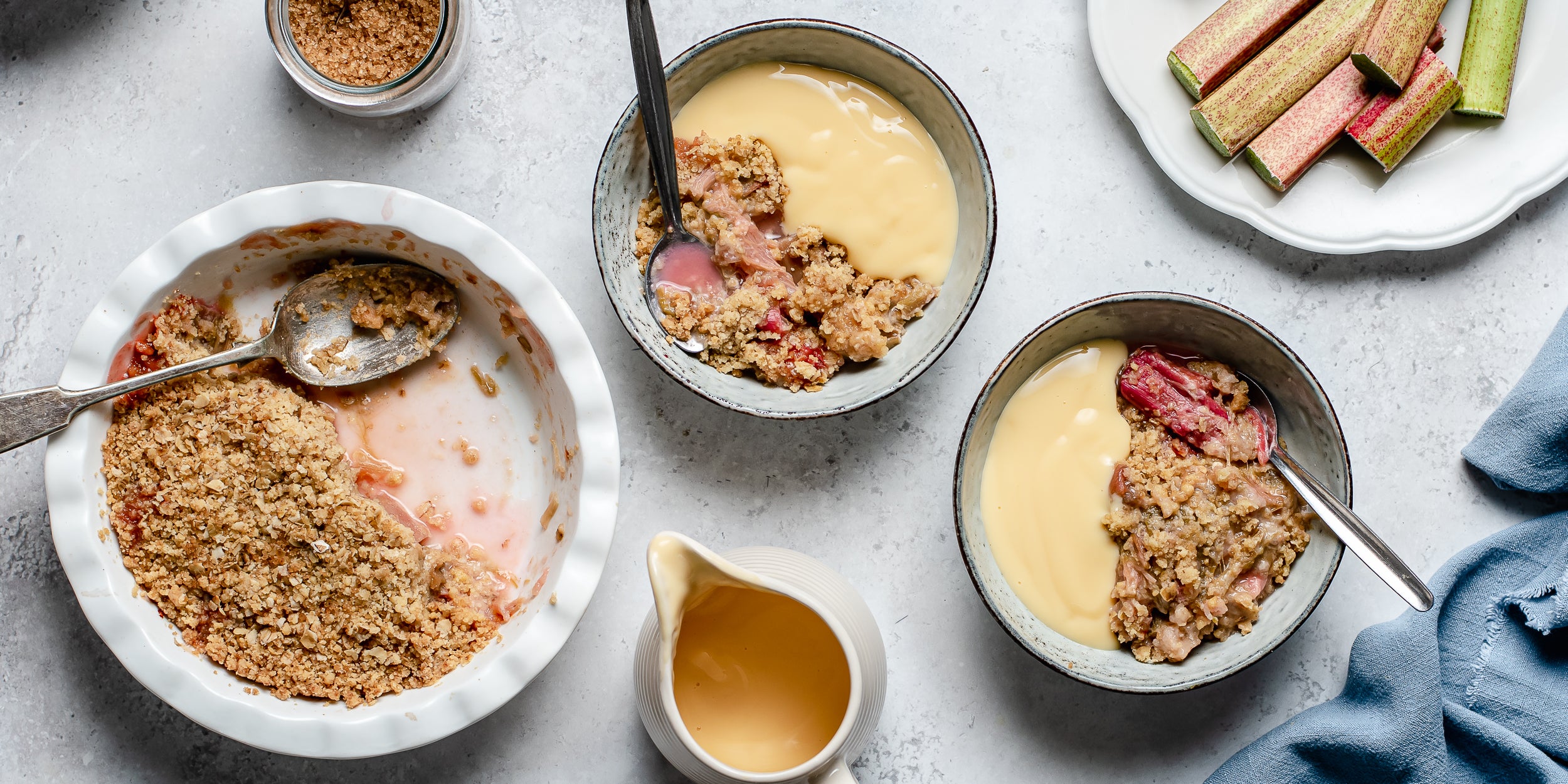 Top view of bowls of warm Rhubarb Crumble topped with vanilla custard ready to serve