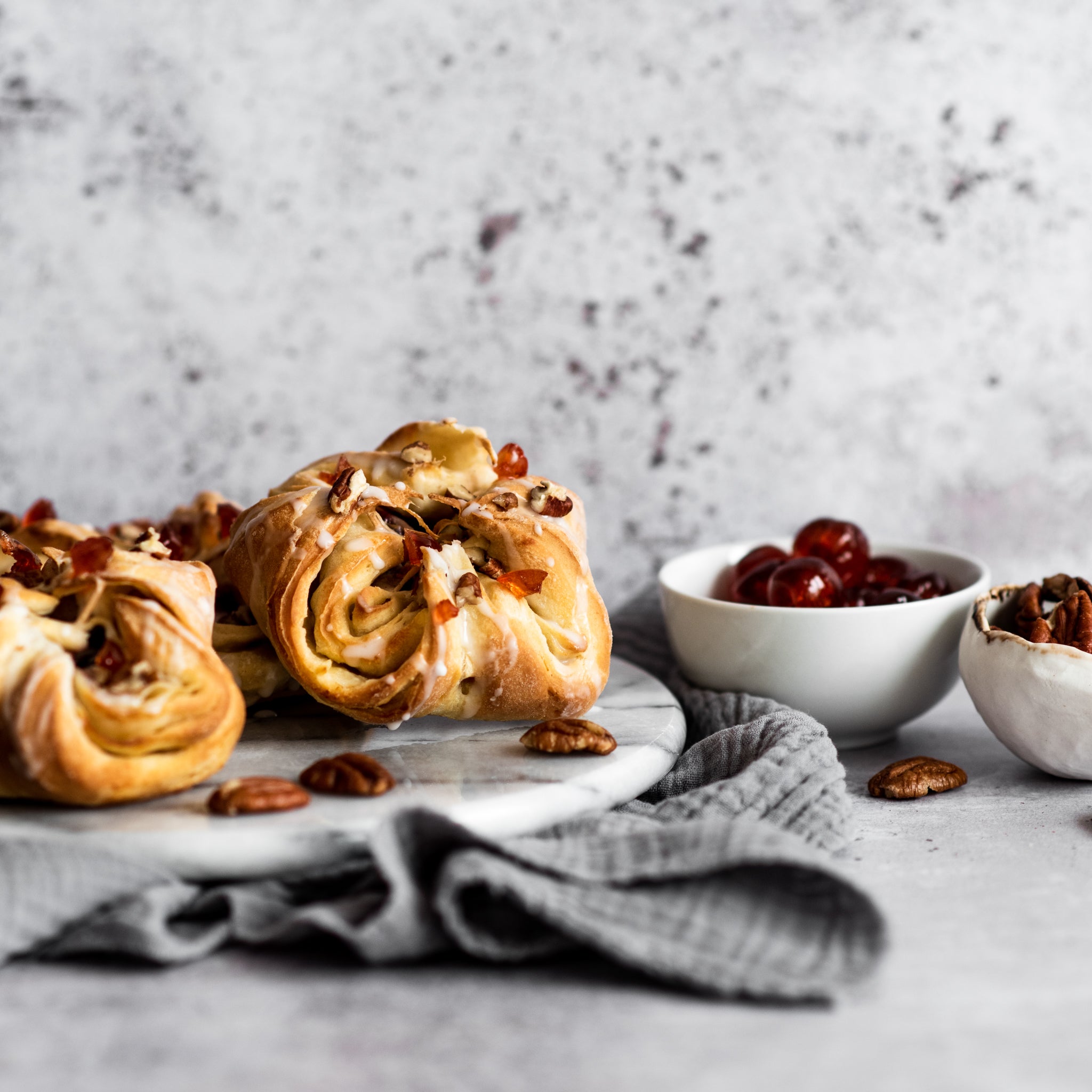 Close up of two danish pastries and bowl of pecans and cherries