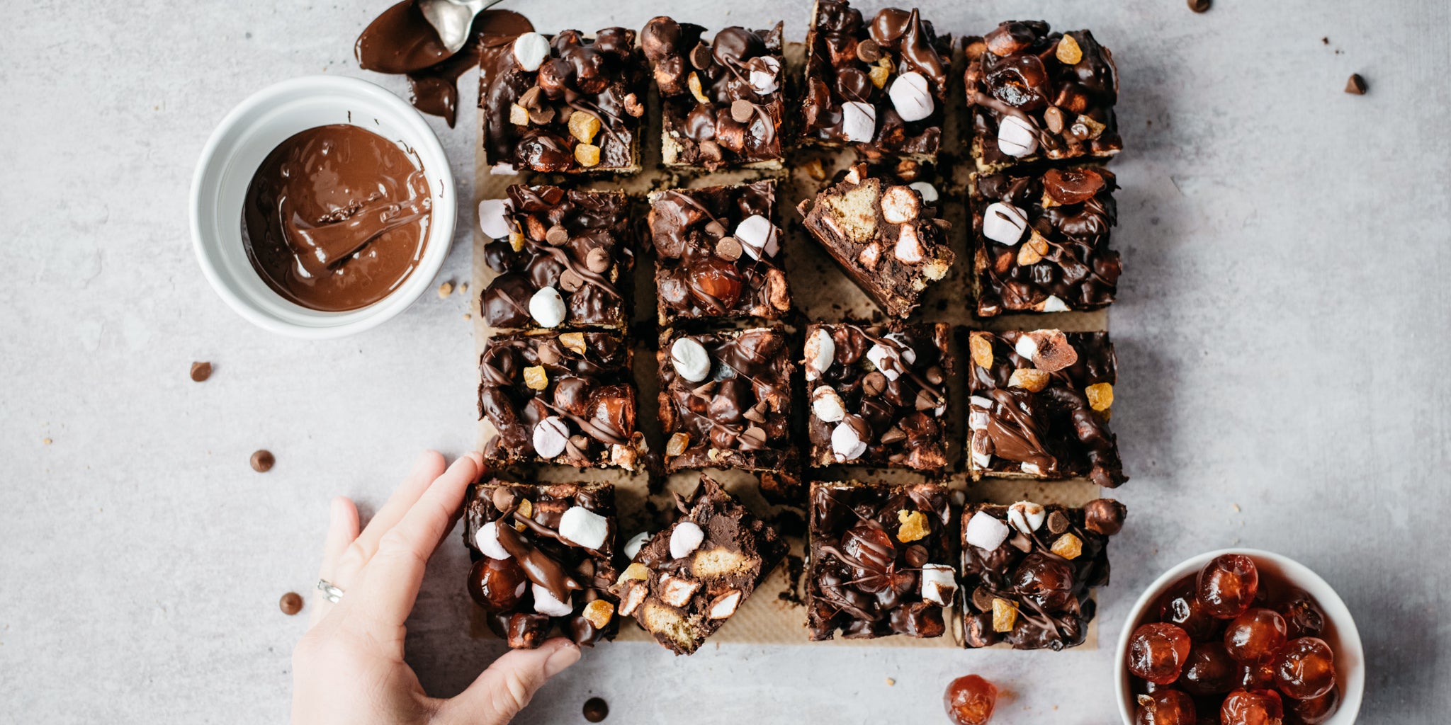 Top view of a Vegan Rocky Road traybake cut into squares, with a hand reaching for one
