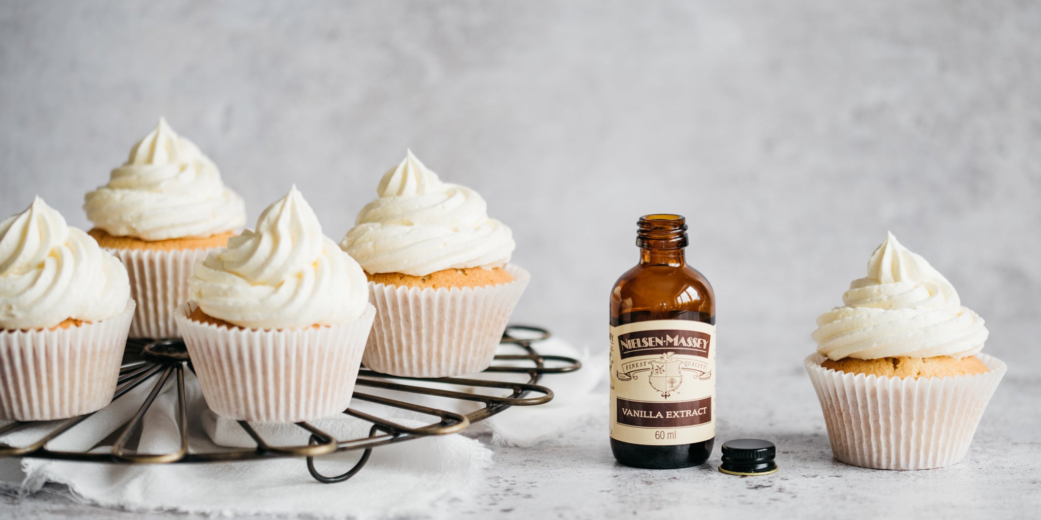 Batch of Vanilla Extract Cupcakes on a wire rack. next to a bottle of Nie4lsen Massey Vanilla extract