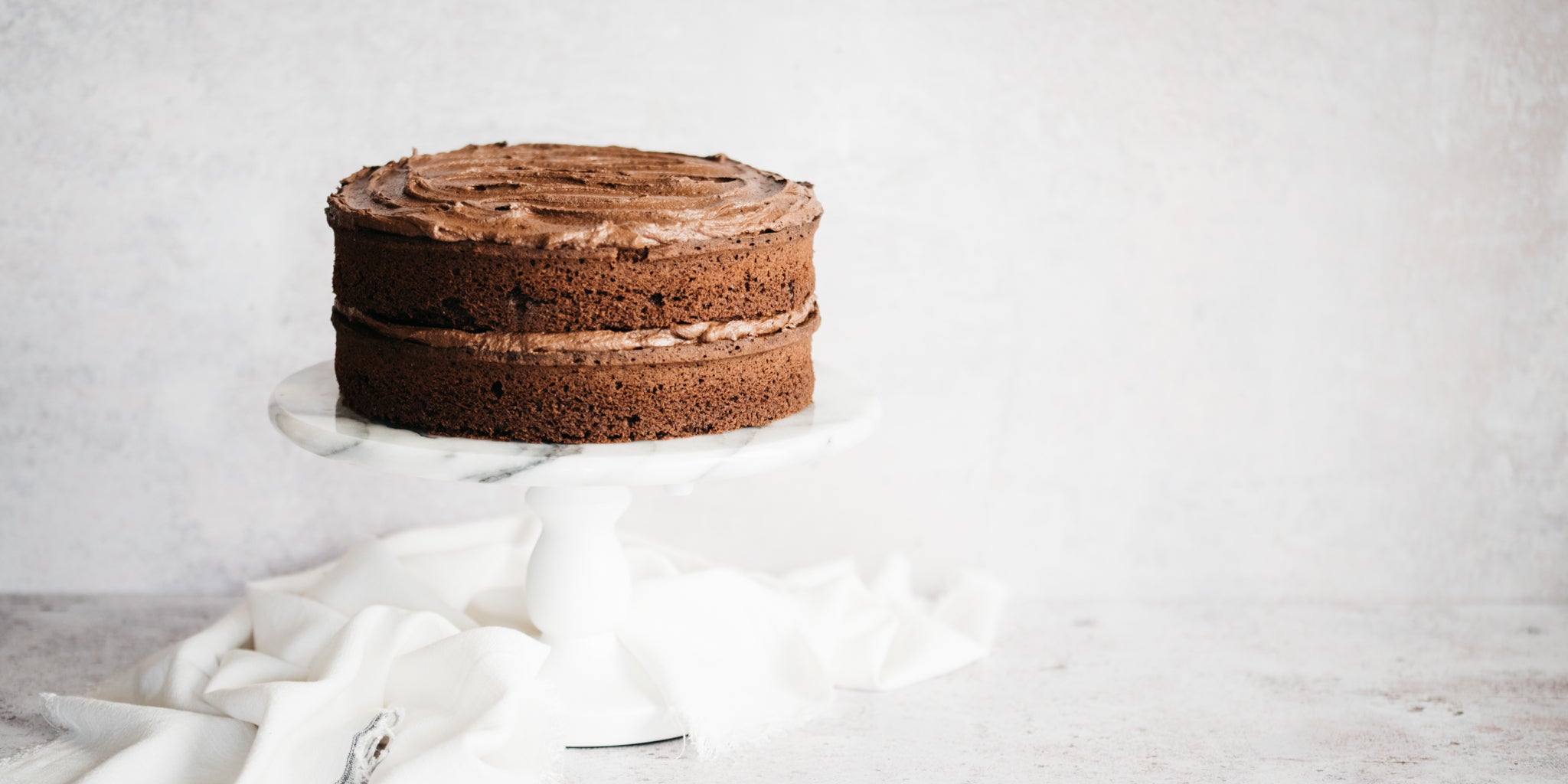 Chocolate cake topped with buttercream on a white cake stand