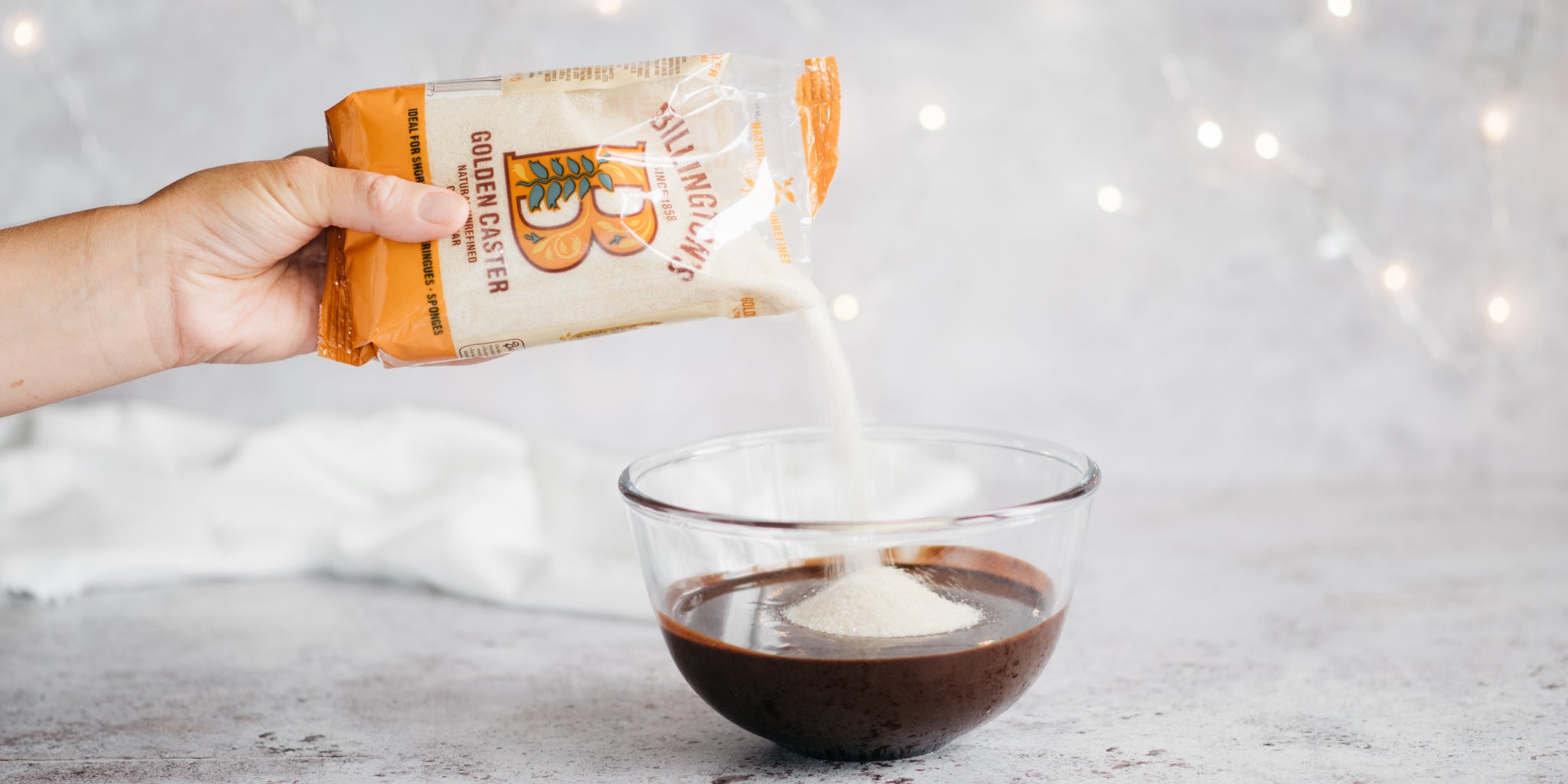 Sugar being poured from a bag into a clear bowl of melted chocolate