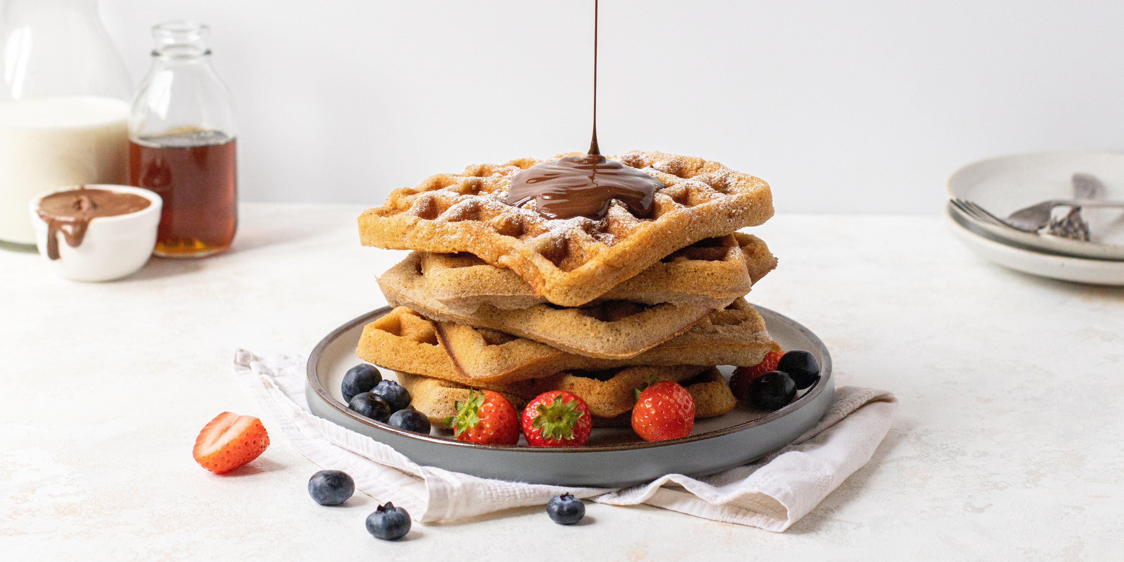 Stack of waffles being drizzled in chocolate sauce, topped with fresh berries