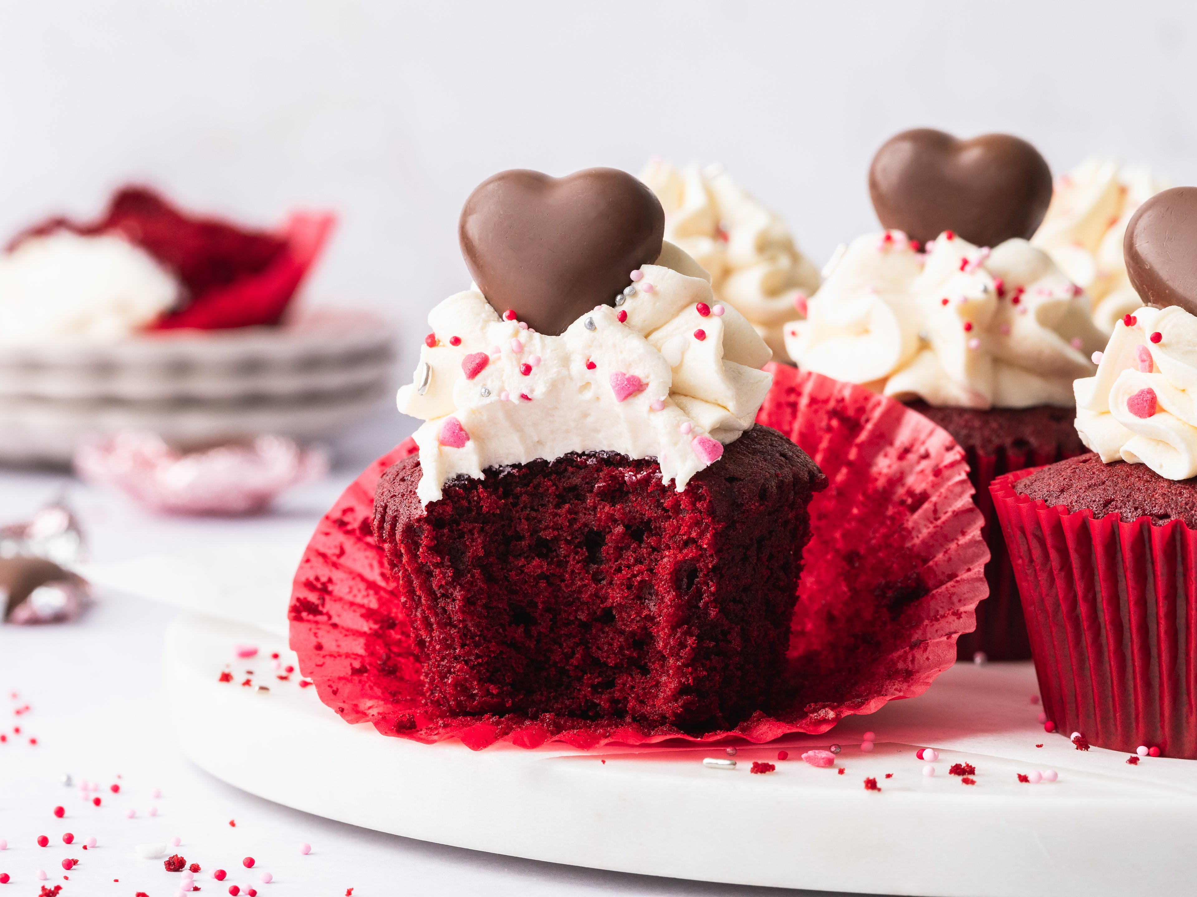 Red velvet cupcake with wrapper peeled back and a bite take out of it. 