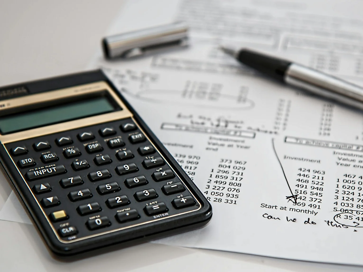 Financial calculator placed on printed investment spreadsheets with a pen