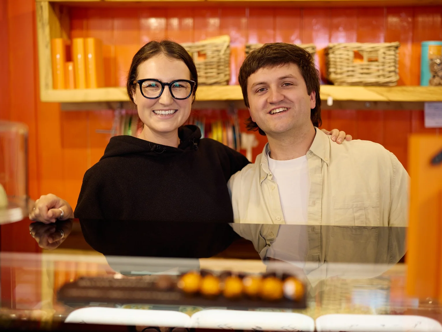 Two young people smiling behind the counter of a colourful confectionery shop