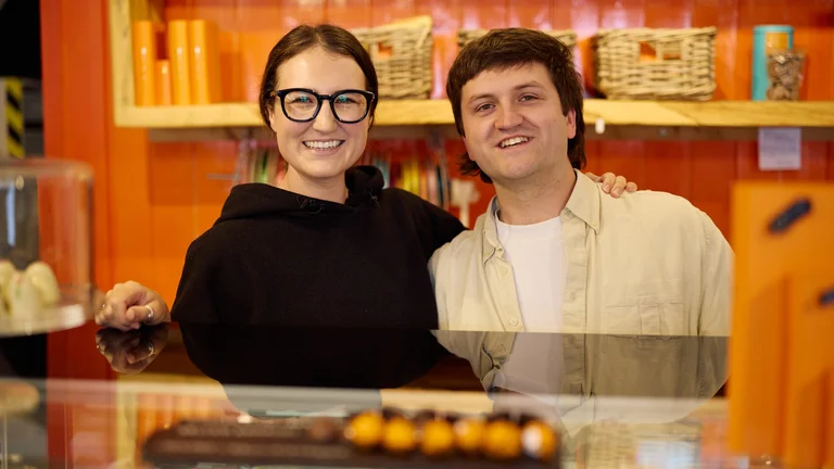 Two young people smiling behind the counter of a colourful confectionery shop
