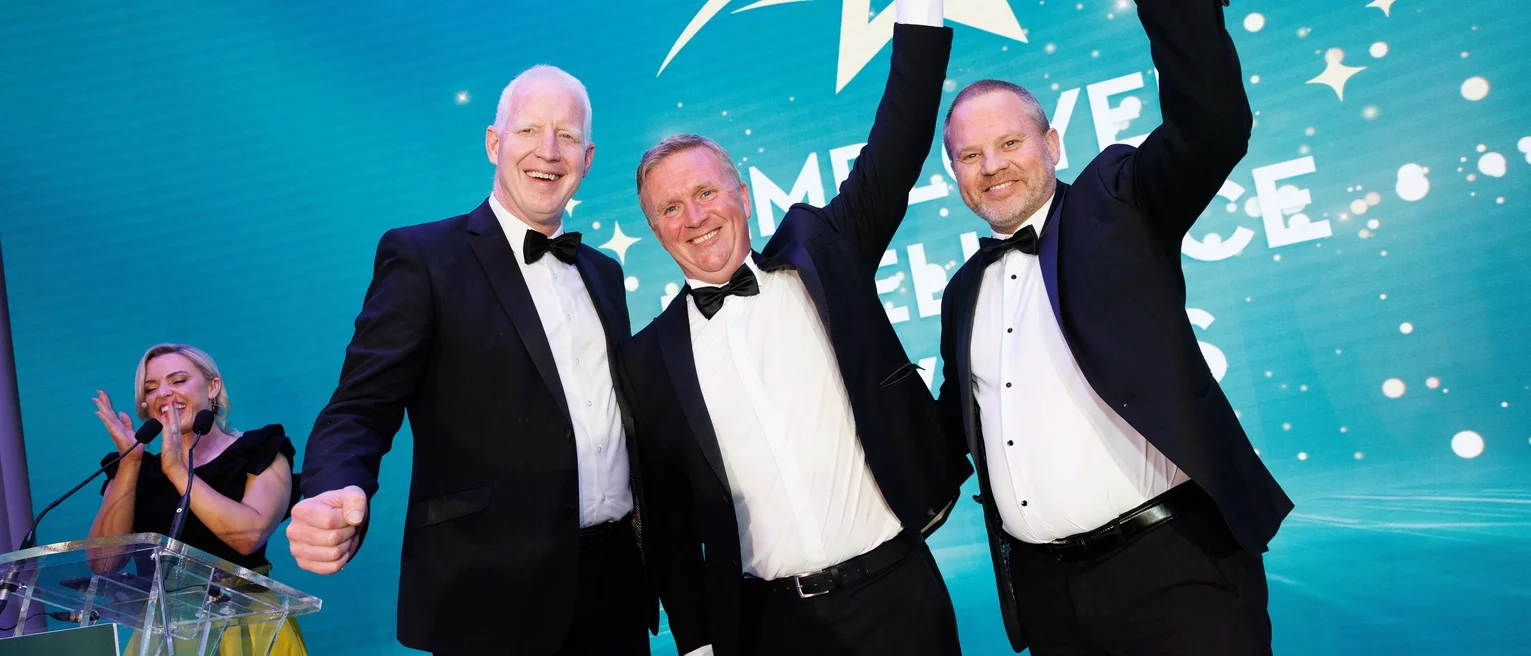 Winners of the employer excellence awards pose for a photo raising fists to the air.