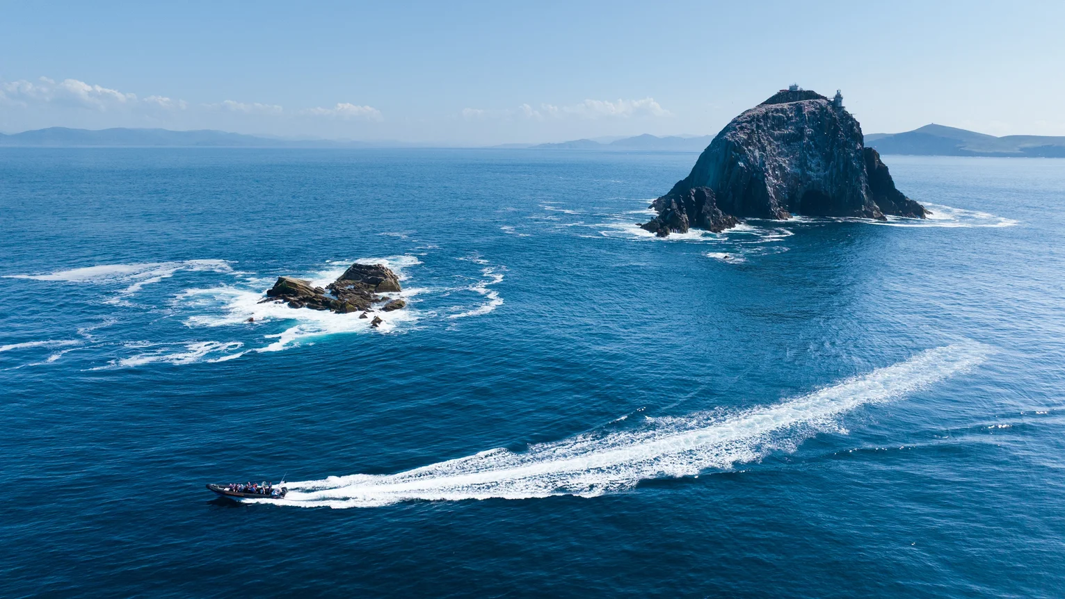 Boat speeding across the ocean leaving a wake near a rocky island