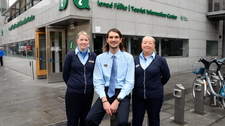 Three staff members standing outside a Fáilte Ireland tourist information centre