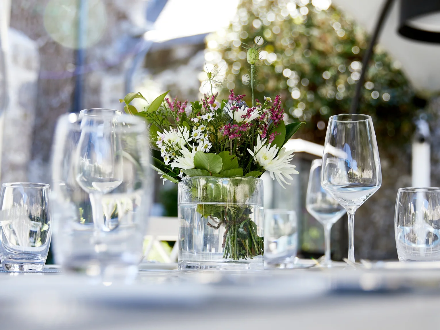 Hotel banquet staff member raising a wine glass to check its clarity in a set dining room with silver candelabras