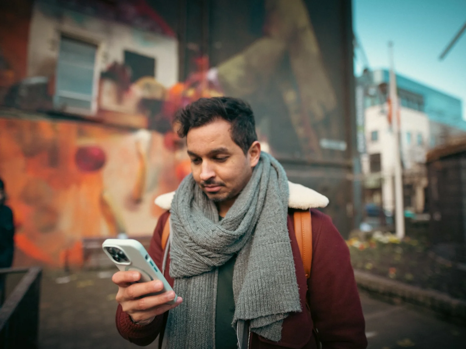 Person looking at their smartphone while standing on a colourful urban street with street art in the background