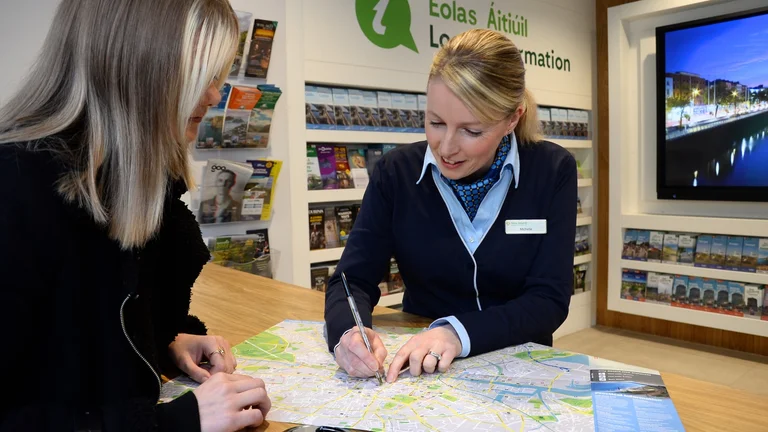 Fáilte Ireland staff member marking a route on a city map while assisting a visitor at an information desk