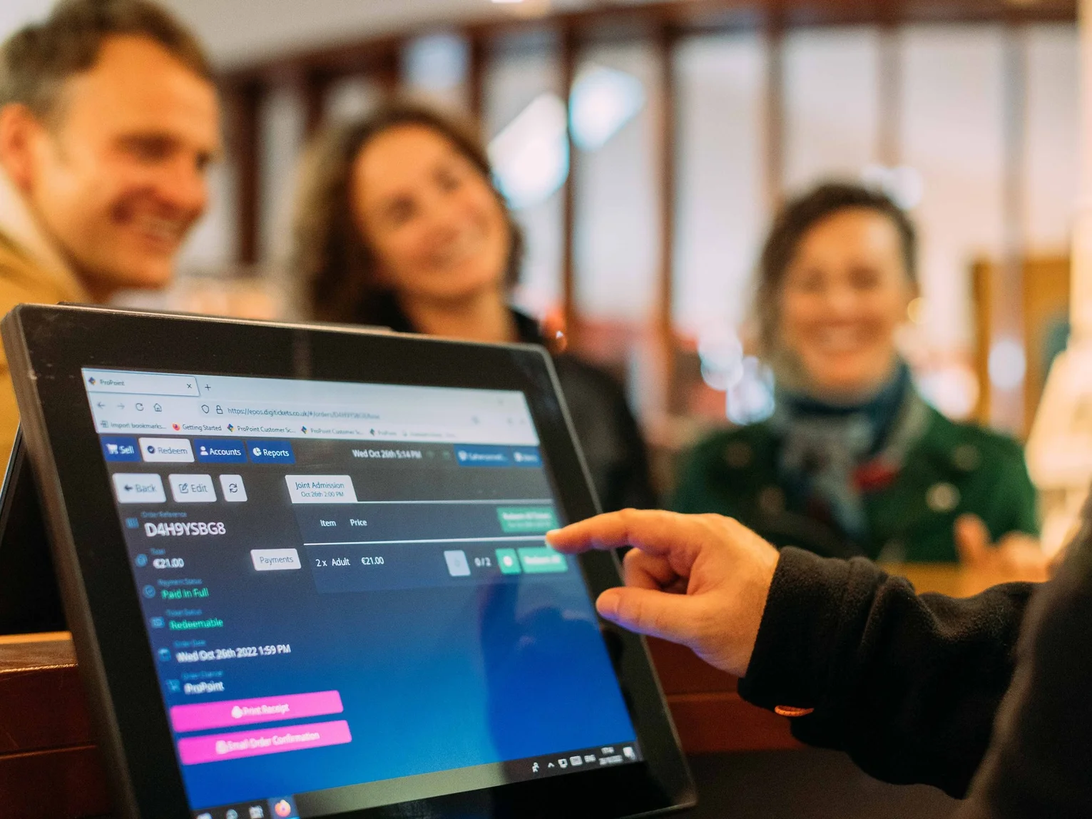Staff member operating a touchscreen point-of-sale and ticketing system, with customers visible in the background