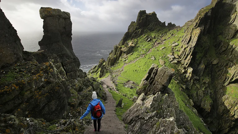 A person walking on a path with a rocky cliff and water in the background