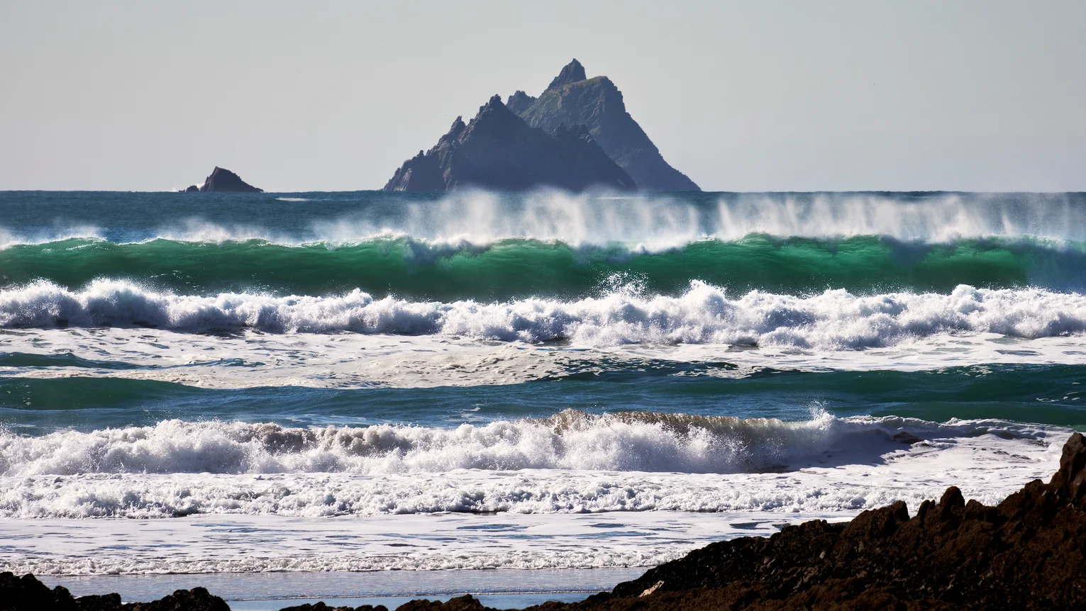 Waves crashing waves on a beach with skellig michael in the background