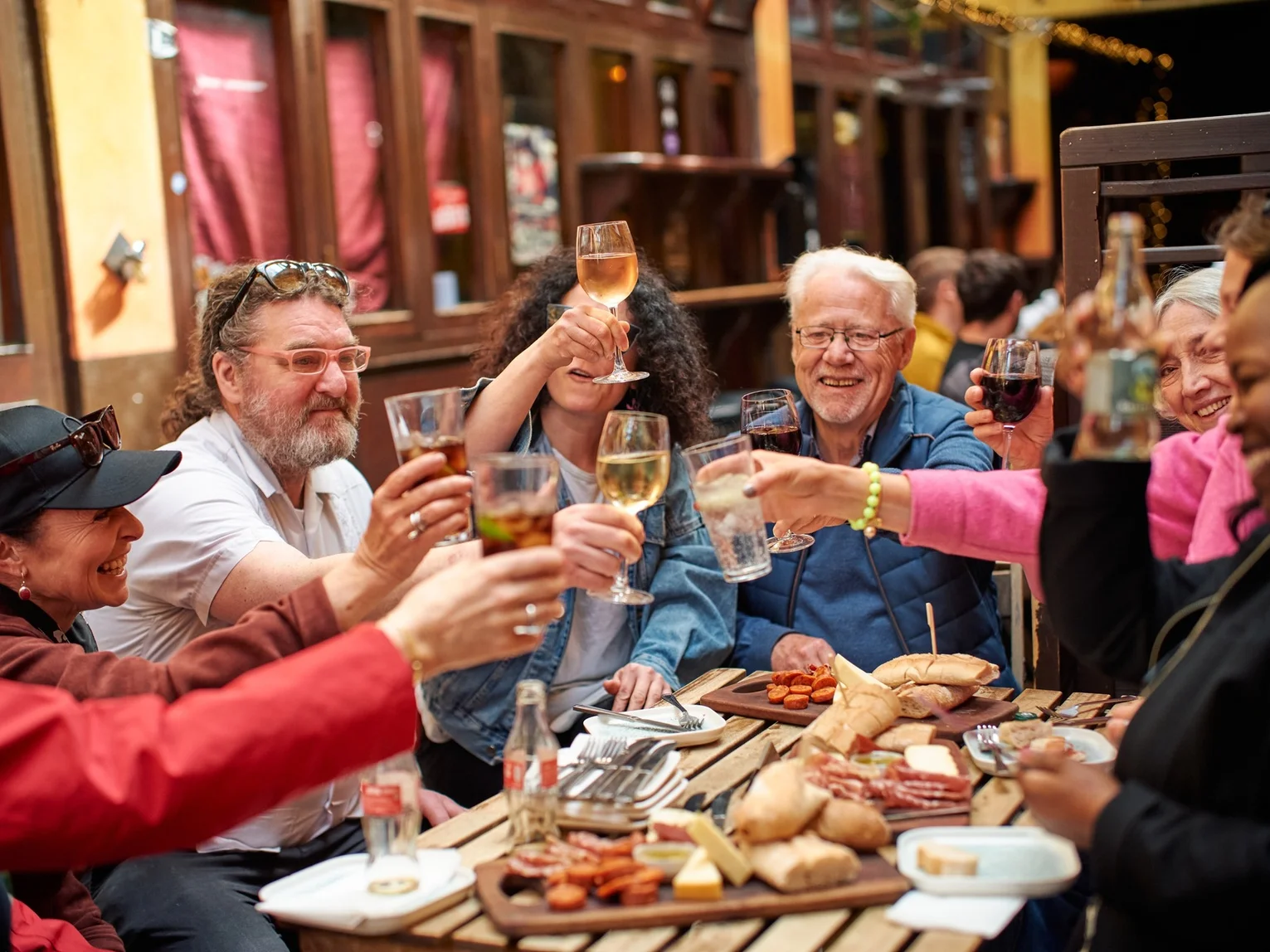 Group of people raising glasses in a toast at an outdoor restaurant table with charcuterie and food boards
