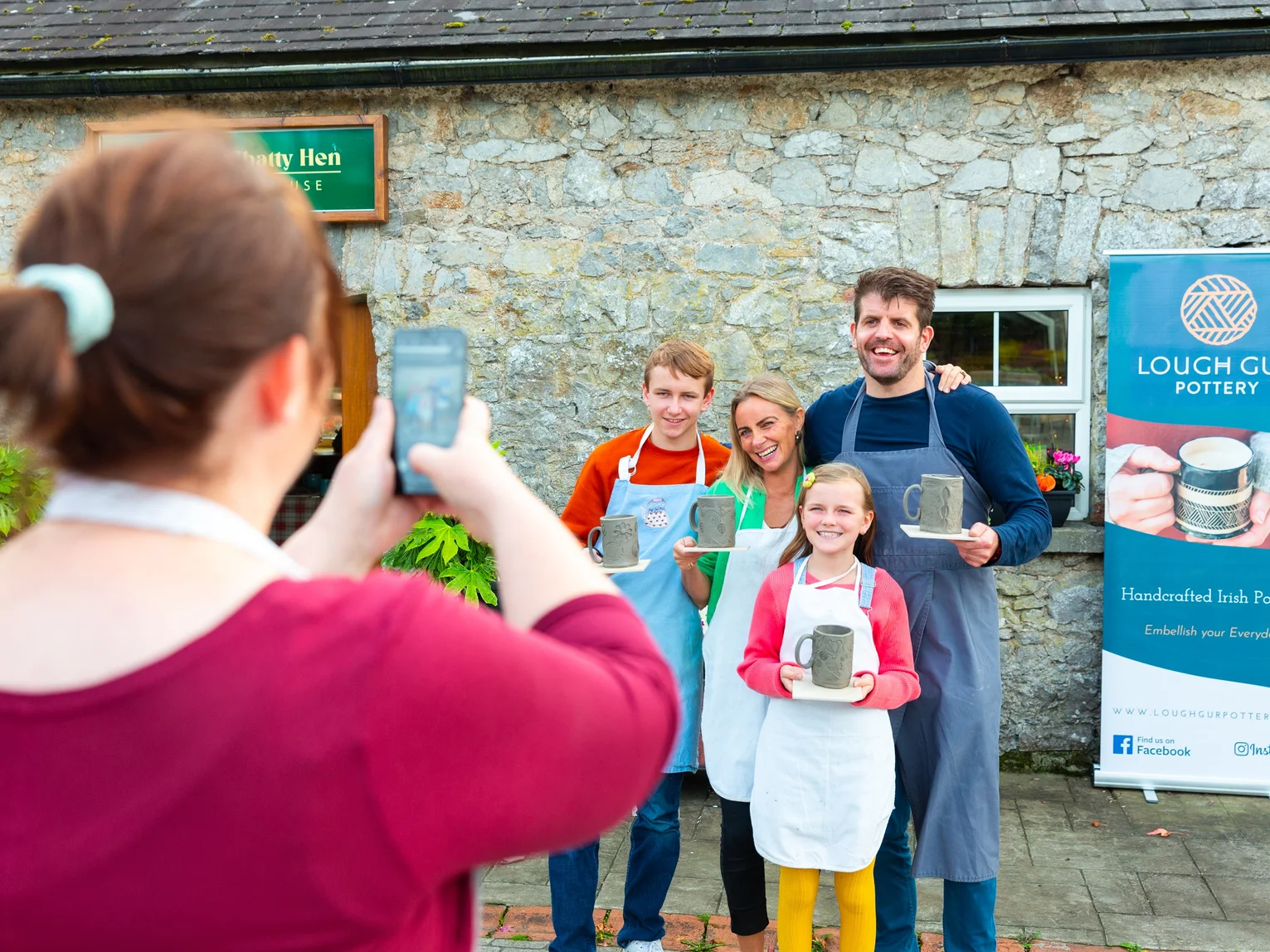 Person using a smartphone to photograph two attendees posing in front of a Fáilte Ireland branded event backdrop