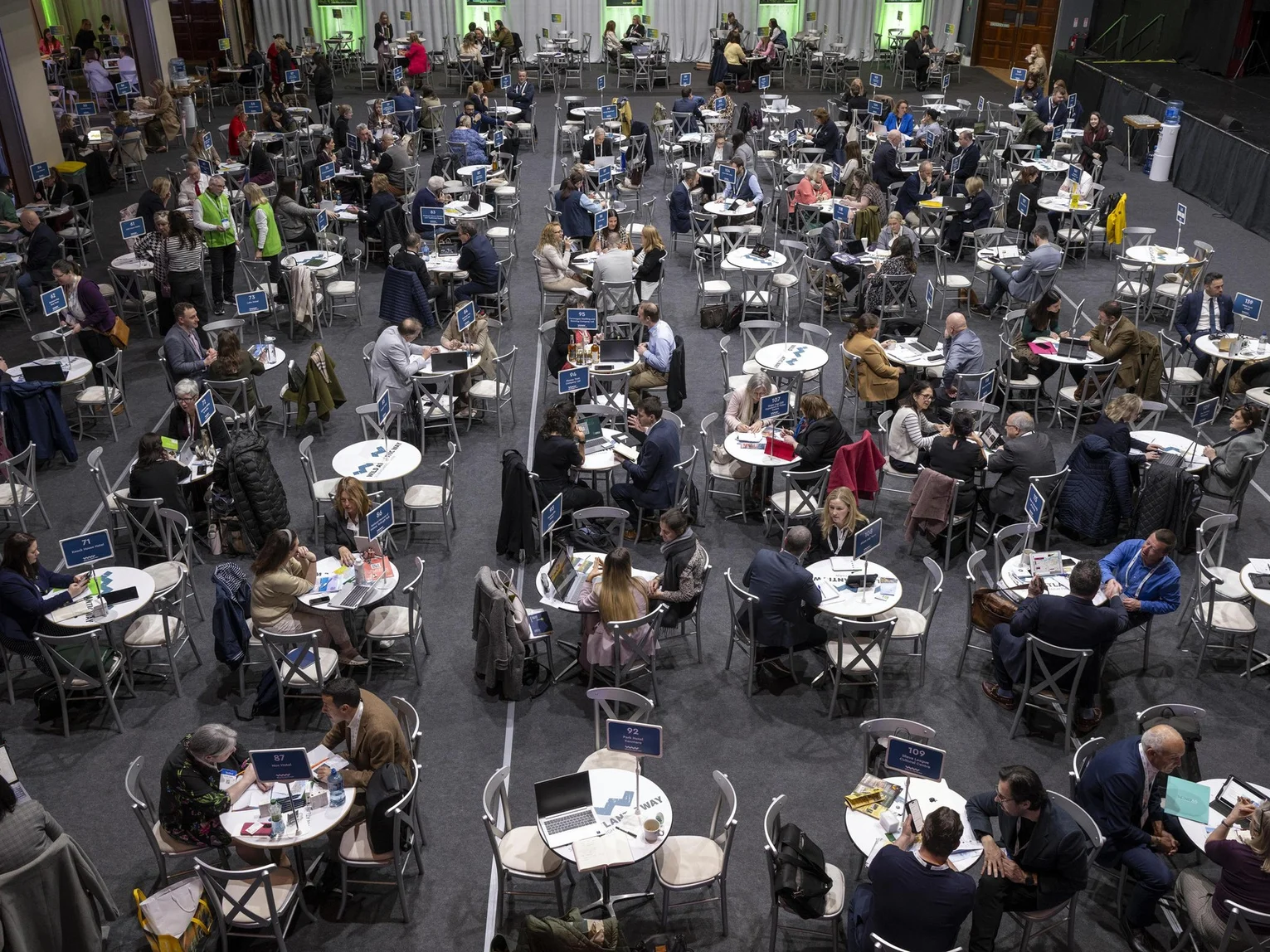 Overhead view of a large trade networking event hall with hundreds of attendees seated at round tables