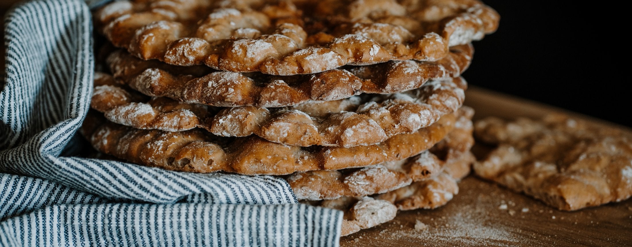 Gestapelte, frisch gebackene Südtiroler Schüttelbrote g.g.A. auf einem Holztisch.
