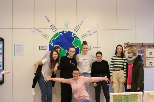 Gruppe von Schülerinnen mit Lehrpersonen stehend vor einem Plakat Gruppe von Schülerinnen mit Lehrpersonen stehend vor einem Plakat