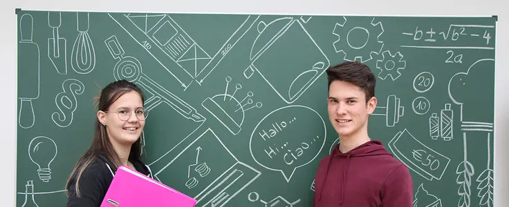 Schülerin mit einer magenta Mappe und Schüler mit Wörterbuch in der Hand vor grüner Schultafel mit Kreidezeichnungen zu verschiedenen Unterrichtfächer Schülerin mit einer magenta Mappe und Schüler mit Wörterbuch in der Hand vor grüner Schultafel mit Kreidezeichnungen zu verschiedenen Unterrichtfächer
