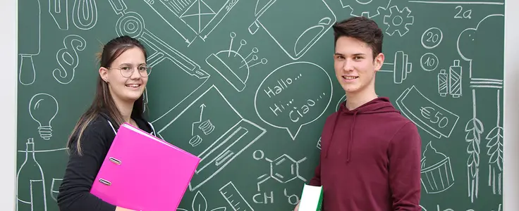Schülerin mit einer magenta Mappe und Schüler mit Wörterbuch in der Hand vor grüner Schultafel mit Kreidezeichnungen zu verschiedenen Unterrichtfächer Schülerin mit einer magenta Mappe und Schüler mit Wörterbuch in der Hand vor grüner Schultafel mit Kreidezeichnungen zu verschiedenen Unterrichtfächer