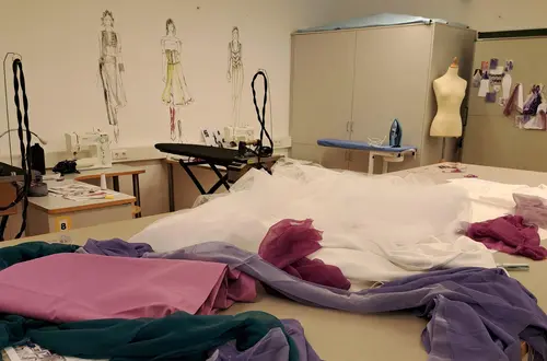 Nährraum: Im Vordergrund der Zuschneidetisch mit verschiedenen Stoffen Nährraum: Im Vordergrund der Zuschneidetisch mit verschiedenen Stoffen