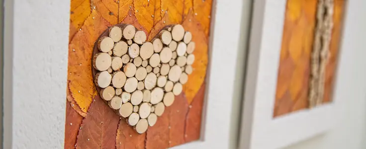 weißer Bilderrahmen mit gepressten Herbstblättern und in der Mitte ein Herz aus verschiedenen großen Holzscheiben weißer Bilderrahmen mit gepressten Herbstblättern und in der Mitte ein Herz aus verschiedenen großen Holzscheiben