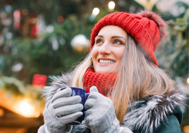 Piros sapkát és kesztyűt viselő nő, kezében kék bögrével