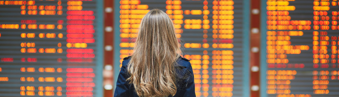 odwołany lot na wyjazd turystyczny, kobieta na tle tablicy lotów na lotnisku, zdjęcie w poziomie