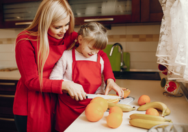 mama z córką kroją owoce w kuchni, czerwony fartuszek