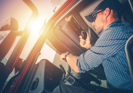Kierowca cięzarówki w koszuli w kratęi okularach przeciwsłonecznych trzyma kierownicę i nadajnik