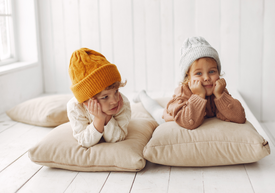 Chłopiec i dziewczynka w czapkach leżą na białym drewnianym podeście na poduszkach