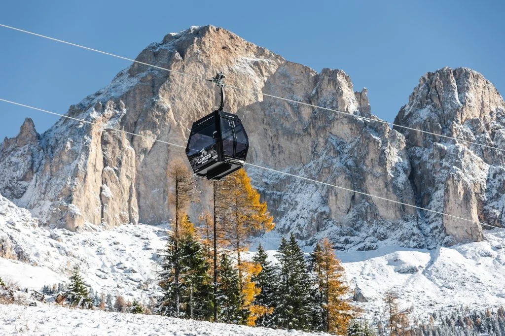 Leitner cable car cabin gliding above snowy slopes in Carezza, with the Dolomite peaks in the background.