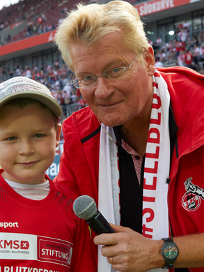 Ein Mann mit Mikrofon steht neben einem Jungen, beide in FC Merch
