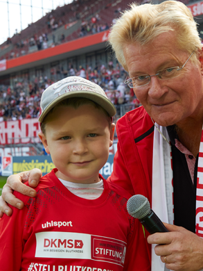 Ein Mann mit Mikrofon steht neben einem Jungen, beide in FC Merch