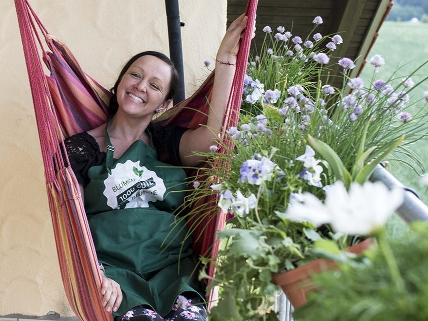 Eine Frau in einer grünen Schürze sitzt in einer Hängematte umgeben von Blumen Eine Frau in einer grünen Schürze sitzt in einer Hängematte umgeben von Blumen