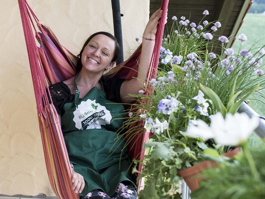 Eine Frau in einer grünen Schürze sitzt in einer Hängematte umgeben von Blumen Eine Frau in einer grünen Schürze sitzt in einer Hängematte umgeben von Blumen