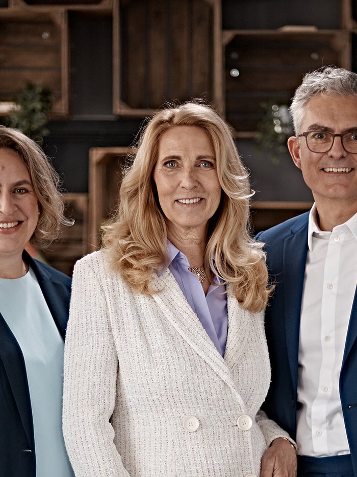 Porträt von Dr. Elke Neujahr, Dr. Deborah Buk und Stephan Schumacher im Business-Outfit vor einem Regal mit Büchern und Dekoration. Porträt von Dr. Elke Neujahr, Dr. Deborah Buk und Stephan Schumacher im Business-Outfit vor einem Regal mit Büchern und Dekoration.