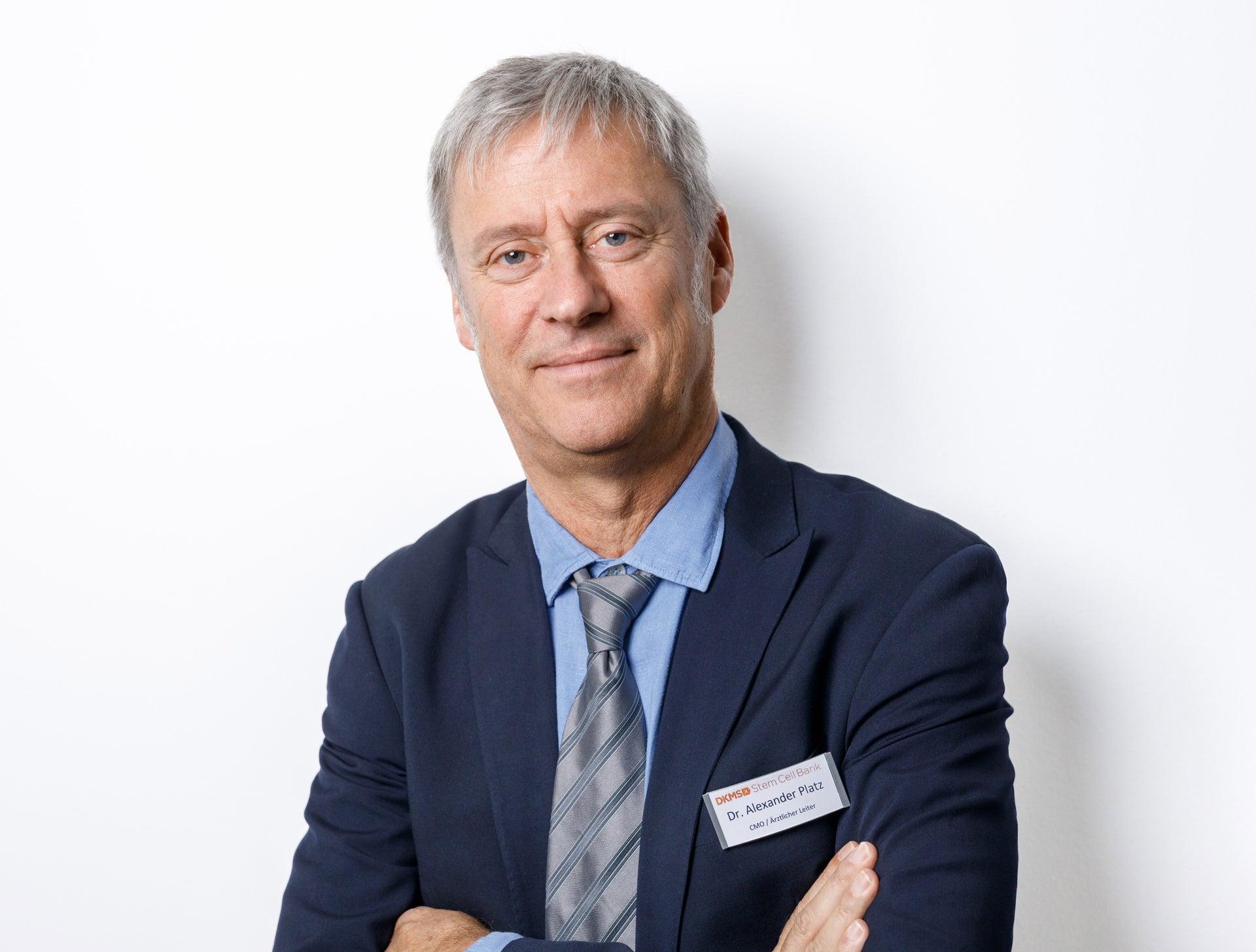 Dr. Alexander Platz im Anzug mit verschränkten Armen Dr. Alexander Platz im Anzug mit verschränkten Armen