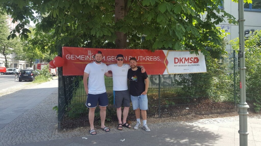 Eine Gruppe von Männern steht vor einem Banner der DKMS. Eine Gruppe von Männern steht vor einem Banner der DKMS.