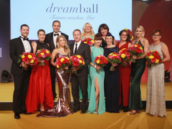Eine Gruppe von Menschen in Kleidern und Anzügen posiert auf dem dreamball für ein Foto. Sie tragen Blumensträuße Eine Gruppe von Menschen in Kleidern und Anzügen posiert auf dem dreamball für ein Foto. Sie tragen Blumensträuße